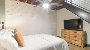 Et soveværelse med en seng, et fjernsyn på en trækommode og et skråt loft.