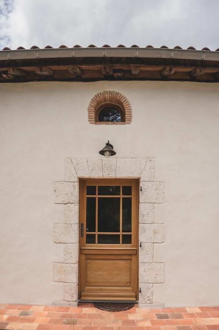 Une entrée d’immeuble avec une porte en bois, un arc en pierre et une petite fenêtre au-dessus de la porte.