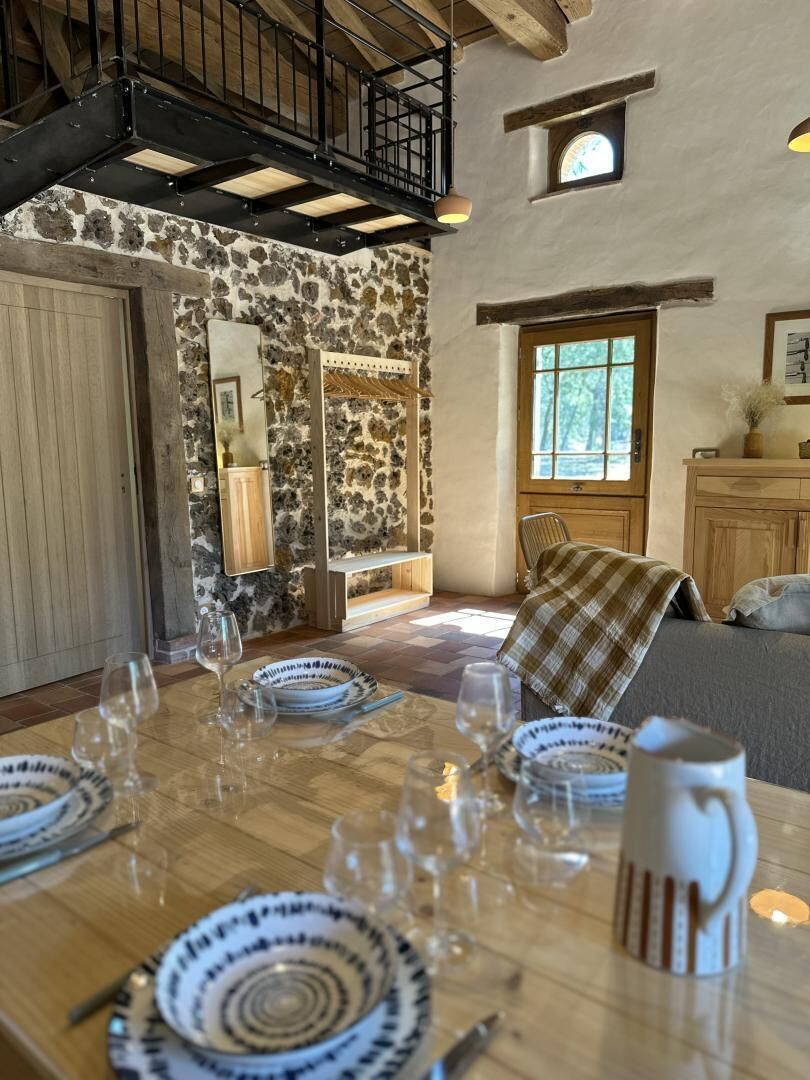 Un coin repas avec une table en bois dressée pour six personnes, des murs en pierre, une porte en bois et un escalier.