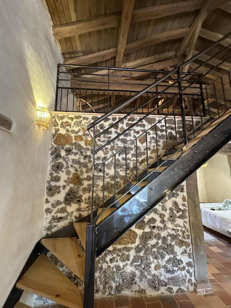 Una escalera con pared de piedra, piso de madera y barandilla de metal.