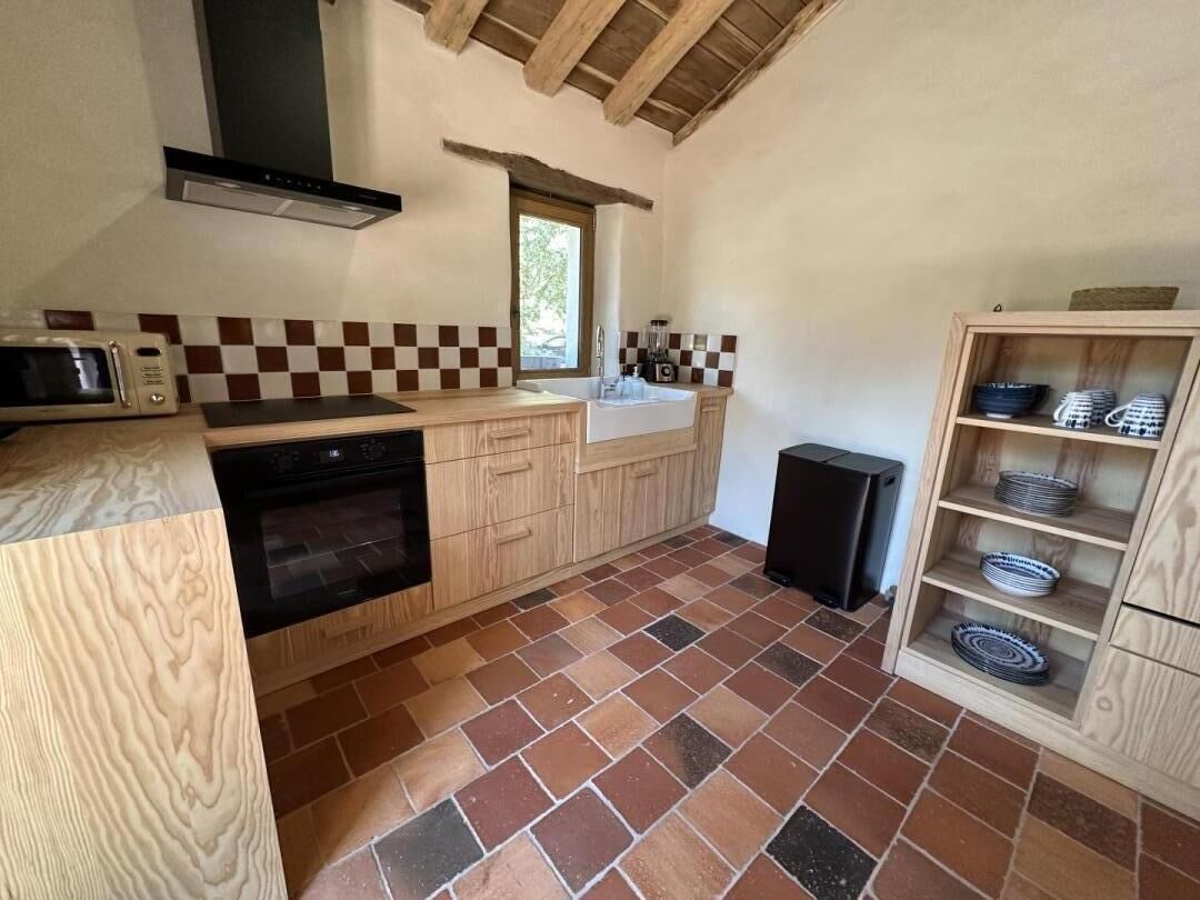 A kitchen with a microwave, oven, and sink. There is a window above the sink and a speaker on the floor.