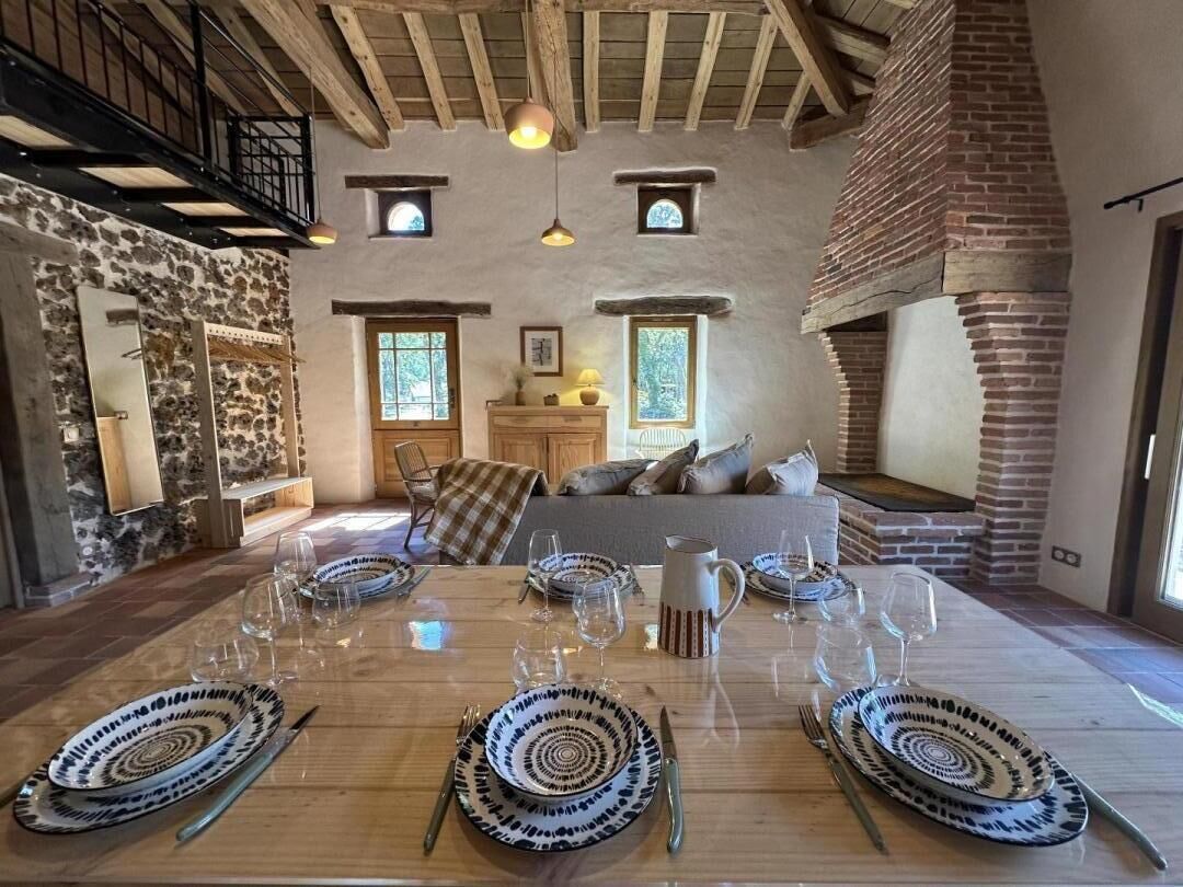 Een eetgedeelte met een houten tafel voor zes personen, een stenen muur, een open haard en een vide met een trap.