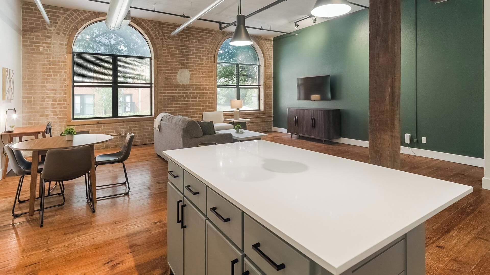 A modern kitchen with a large island, wooden flooring, and a green accent wall.