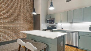 Une cuisine moderne avec un mur en briques, un îlot central doté de sièges et des appareils électroménagers en acier inoxydable.