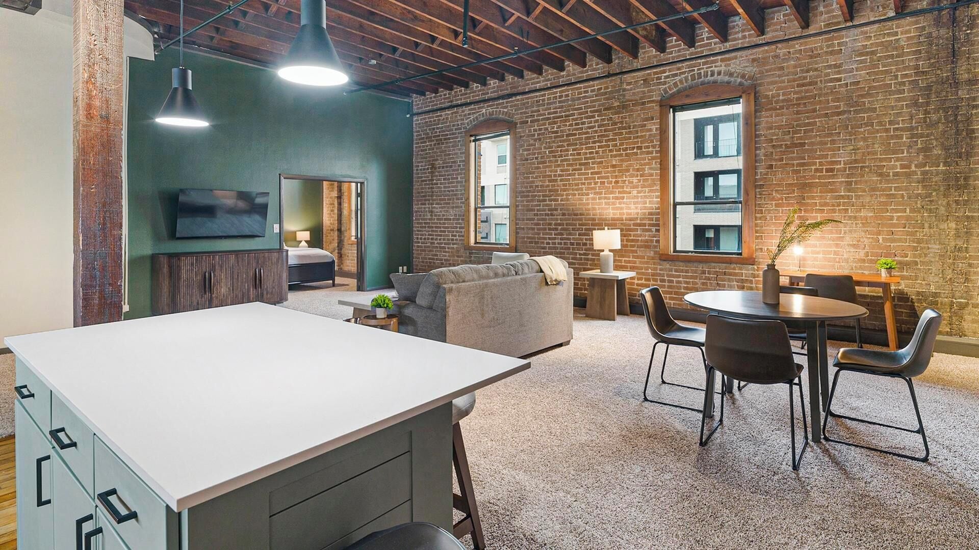 A modern interior with a kitchen area, dining space, and a seating area with a brick wall and large windows.