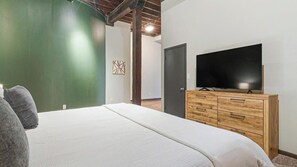 A bedroom with a bed, a TV on a wooden dresser, and a green wall. - Landing | Stylish 2BD, Courtyard, Gym (Houston)