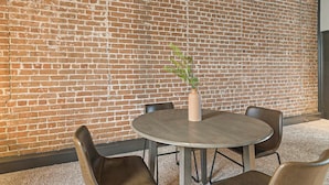 Een ronde tafel met vier stoelen, een vaas met een plant, en een bakstenen muur op de achtergrond.