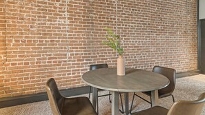 A round table with four chairs, a vase with a plant, and a brick wall in the background. - Landing | Amazing 2BD, Courtyard, Gym (Houston)