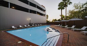 A swimming pool with lounge chairs and umbrellas, a brick pathway, and a modern building with balconies. - Landing | Amazing 2BD, Courtyard, Gym (Houston)