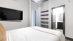 Un dormitorio con una cama, un televisor montado en la pared y una puerta que da a un baño.