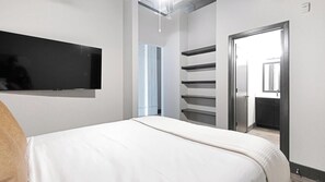 A bedroom with a bed, a TV mounted on the wall, and a door leading to a bathroom. - Landing | Amazing 1BD, Courtyard, Gym (Houston)