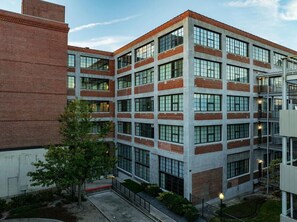A multi-story building with a brick facade, large windows, and a courtyard with trees. - Landing | Incredible 1BD, Gym, Courtyard (Houston)