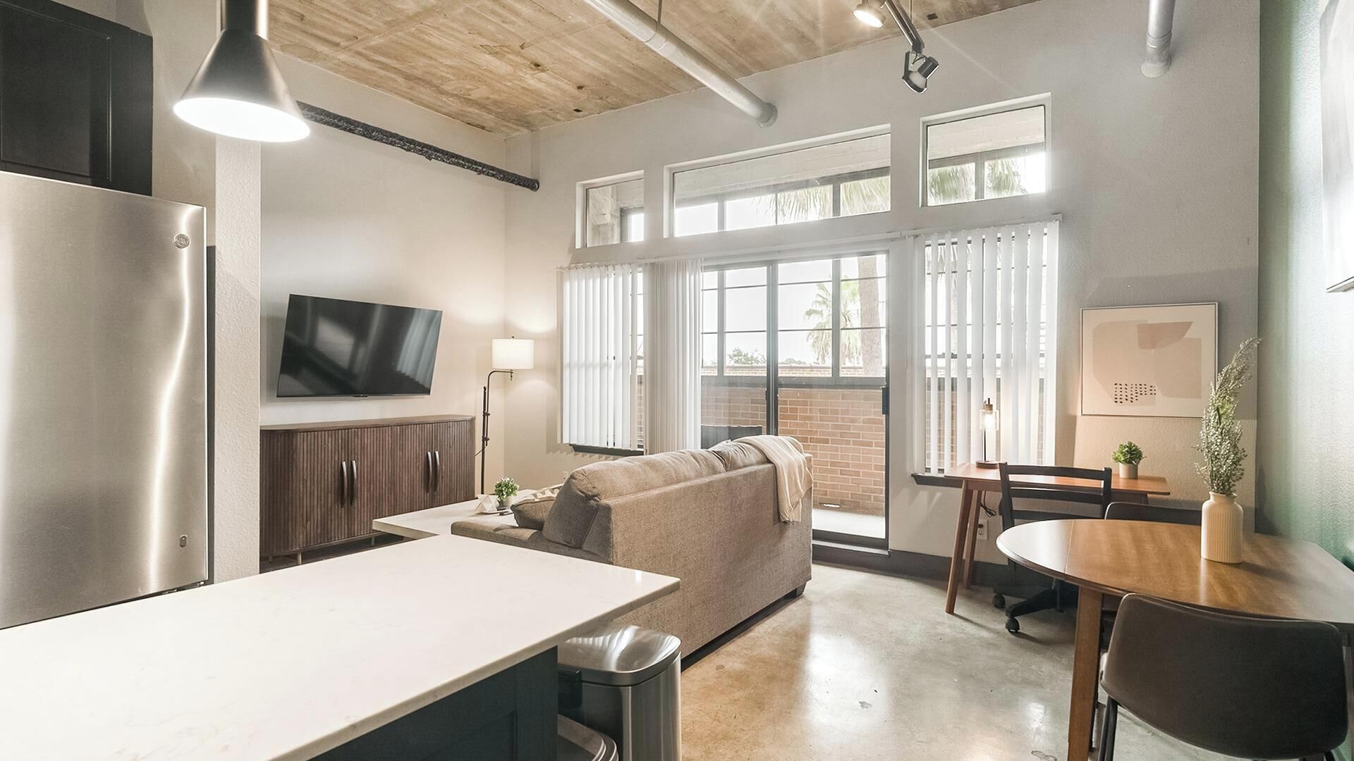A modern kitchen with a stainless steel refrigerator, a flat-screen TV, and a dining area with a table and chairs.