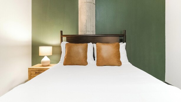 Una cama bien hecha con dos almohadas, una lámpara de noche y una mesita de madera.