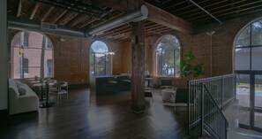 A spacious interior with brick walls, large windows, and a wooden ceiling. - Landing | Amazing 2BD, Gym, Courtyard (Houston)
