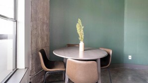 Una mesa pequeña y redonda con un florero, dos sillas y una pared verde.