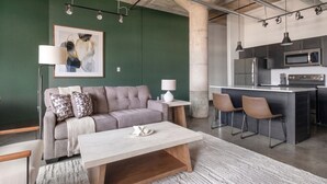 Un espacio habitable moderno con un sofá, una mesa de centro y una cocina equipada con microondas y sillas.