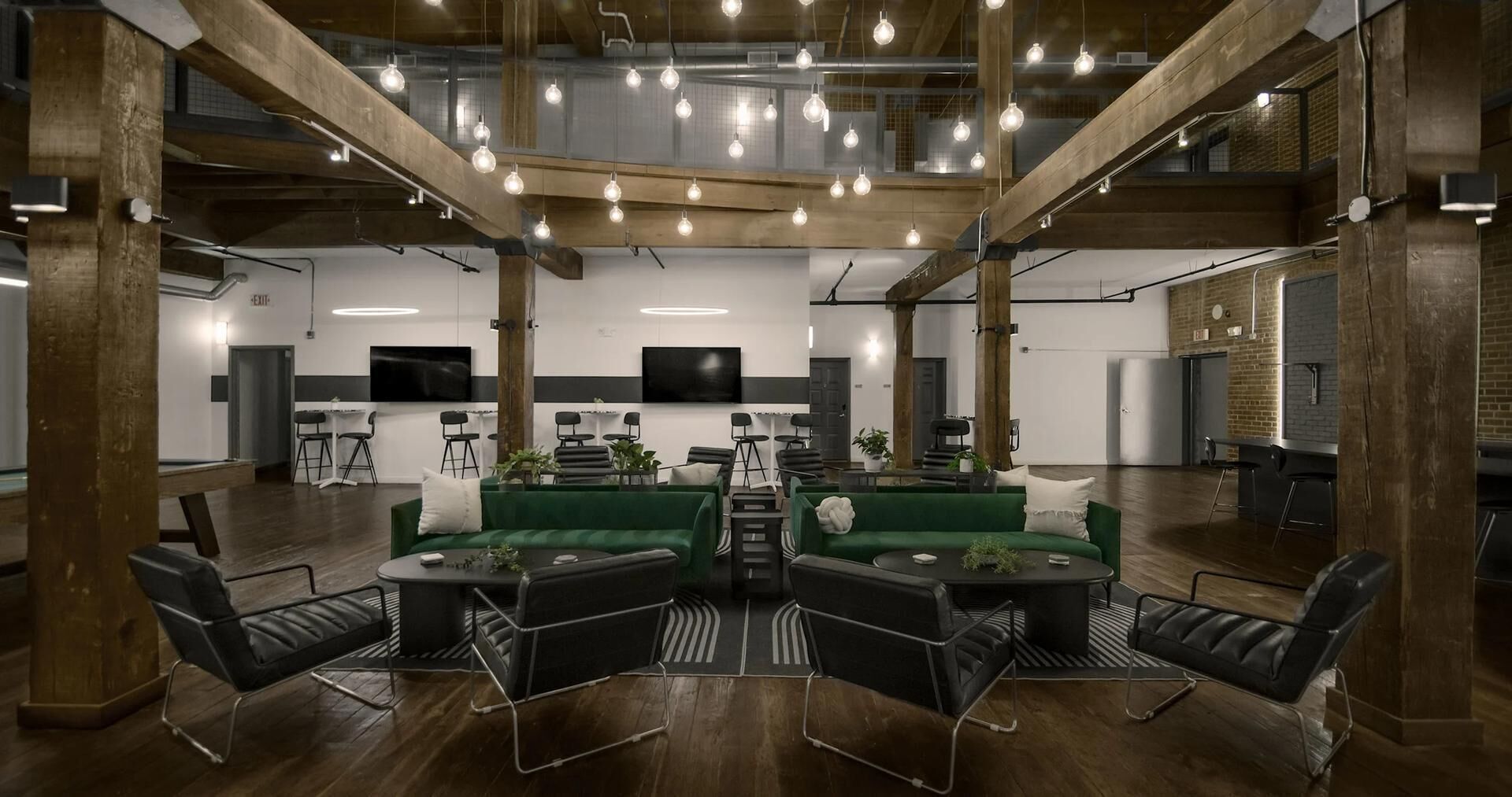 A spacious lounge with high ceilings, exposed beams, and hanging light fixtures.