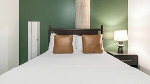 Une chambre d’hôtel avec un lit, deux oreillers, une table de chevet avec une lampe et une armoire.