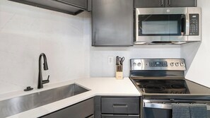 A modern kitchen with stainless steel appliances, a sink, and a knife block. - Landing | Amazing 1BD, Courtyard, Gym (Houston)