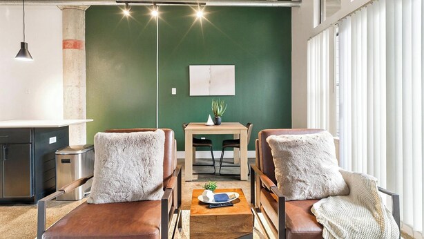 Un salon moderne avec deux fauteuils en cuir, une table basse en bois et un mur d’accent vert.