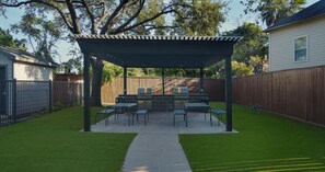 A backyard with a covered patio, grilling area, and outdoor seating. - Landing | Amazing 1BD, Courtyard, Gym (Houston)