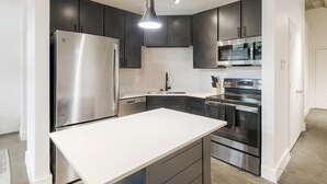 Une cuisine moderne dotée d’appareils électroménagers en acier inoxydable, de meubles de rangement aux couleurs sombres et d’un plan de travail blanc.