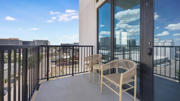 A balcony with a view of the city, two wicker chairs, and a glass door. - Landing | Stylish 2BD, Gym, Yoga Studio (Denver)