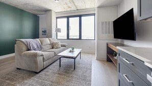 A modern living room with a sofa, a coffee table, and a TV mounted on the wall. - Landing | Amazing 1BD, Gym, Yoga Studio (Denver)