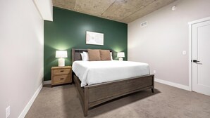 Een slaapkamer met een bed, nachtkastjes, een kunstwerk aan de muur en een deur.
