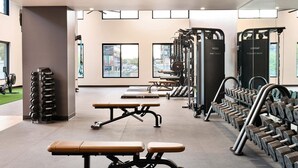 Ett gym med utrustning för styrketräning, träningsbänkar och en utsikt över staden genom stora fönster.