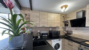 Uma cozinha moderna com armários de madeira, micro-ondas, máquina de lavar e um vaso com planta.