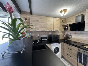 Eine moderne Küche mit Holzschränken, einer Mikrowelle, einer Waschmaschine und einem Blumentopf.