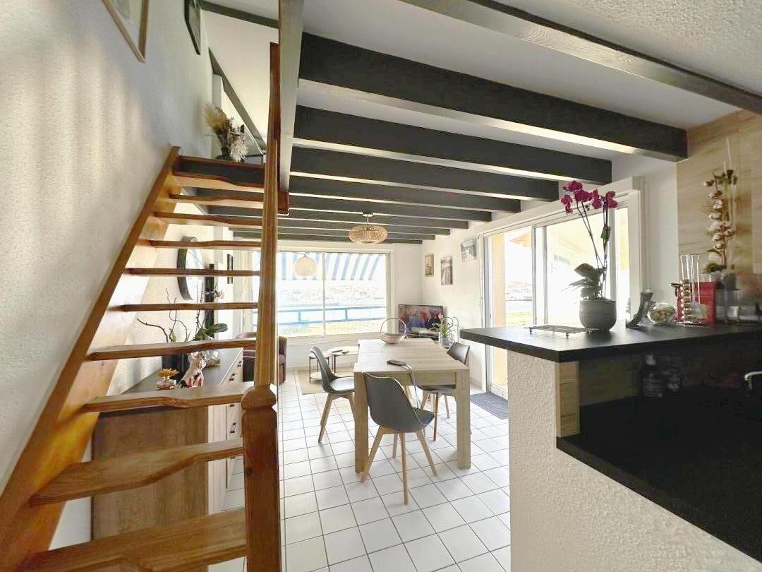 A modern kitchen with a wooden staircase, a dining area with a table and chairs, and a view through a large window.