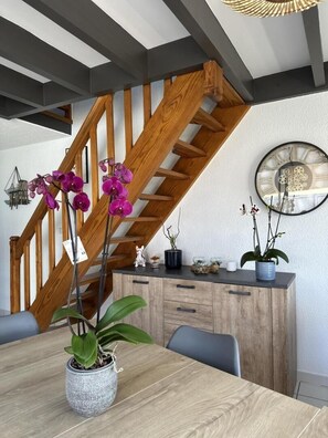 A dining area with a wooden staircase, a table with chairs, and potted plants. - Gîte du Courant - MIMIZAN (MIMIZAN)