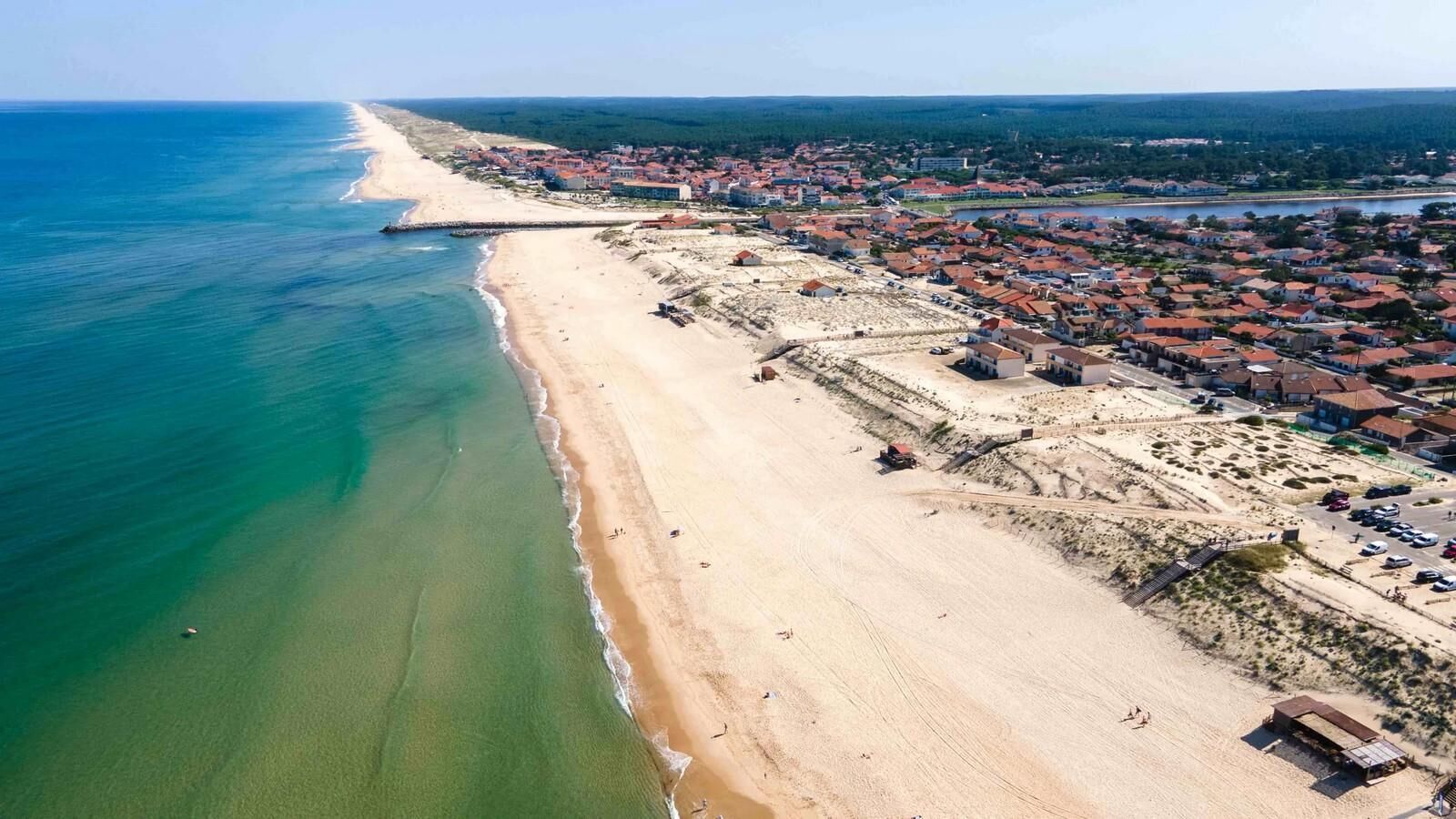 An aerial view of a coastal town with a beach, residential buildings, and a clear sky.