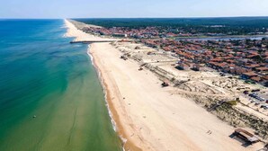 Vista aérea de uma vila costeira com praia, edifícios residenciais e céu claro.
