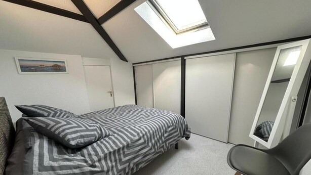 Quarto com cama, cadeira, claraboia, guarda-roupa e porta.
