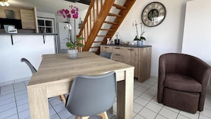 Uma área de refeições com mesa e cadeiras de madeira, uma escada, um espaço de cozinha e uma poltrona marrom.
