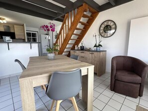 Ein Essbereich mit Holztisch und Stühlen, eine Treppe, ein Küchenbereich und ein brauner Sessel.
