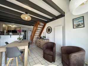 Et moderne køkken med en trætrappe, et spiseområde med et træbord og stole, og en opholdsstue med to brune lænestole.