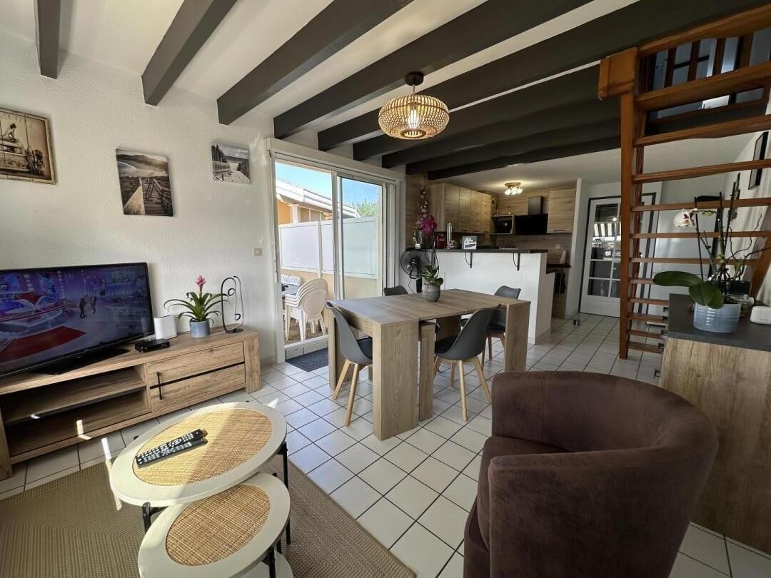 A living room with a TV, dining table, and chairs, a kitchen in the background, and a staircase leading to another level.