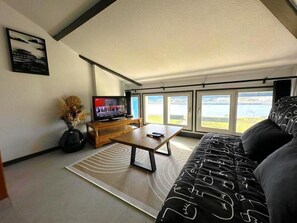 Ein Wohnzimmer mit einer Couch, einem Couchtisch, einem Fernseher und Blick ins Freie.