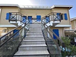 Eine Treppe führt nach draußen zu einem Gebäude mit blauen Fensterläden und einem Glasgeländer.