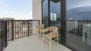 A balcony with two wicker chairs, a glass door, and a view of the cityscape. - Landing | Amazing 2BD, Yoga Studio, Gym (Denver)