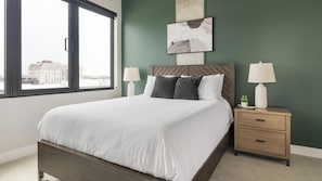 Ein Schlafzimmer mit einem Bett, Nachttischen, einem Fenster und Blick auf die Stadt.