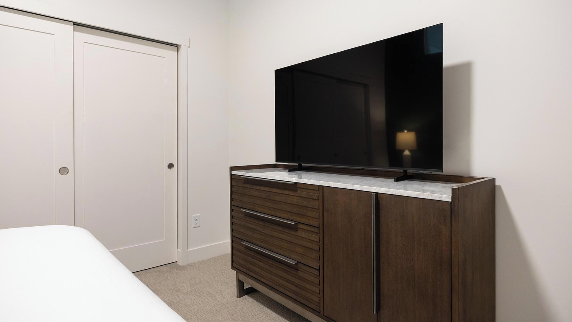 Un dormitorio con cama, cómoda con cajones, televisor de pantalla plana montado en la pared y armario.