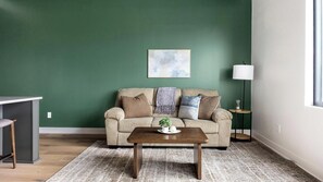 A living room with a green wall, a striped sofa, a wooden coffee table, and a floor lamp. - Landing | Chic 1BD, Clubhouse, Yoga Studio (Denver)