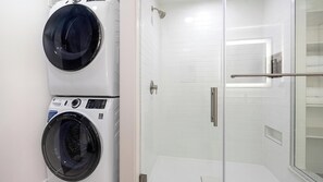 A laundry area with two washing machines and a glass-enclosed shower stall. - Landing | Chic 1BD, Clubhouse, Yoga Studio (Denver)
