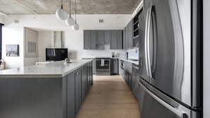 A modern kitchen with grey cabinetry, stainless steel appliances, and pendant lighting.
